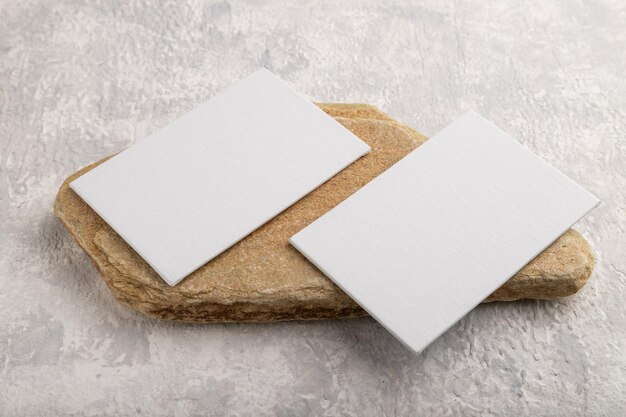 Photo white paper business card mockup with stone on gray concrete background side view canvas copy space