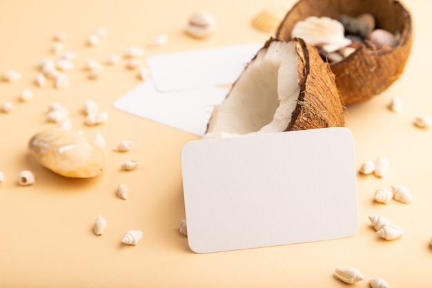 white paper business card with coconut and seashells on orange pastel background. copy space. 