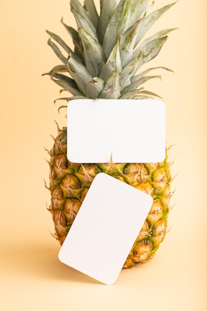 Визитная карточка из белой бумаги со спелым ананасом на оранжевом пастельном фоне, вид сбоку