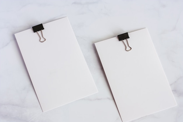 White paper card with binder clip on white marble background