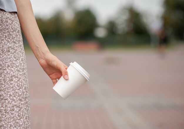 Tazza di carta bianca con caffè in mano della donna. tempo per bere un caffè in città. caffè da portar via. goditi il momento, prenditi una pausa. primo piano della tazza di carta usa e getta. bevanda calda deliziosa. spazio vuoto per testo, mockup