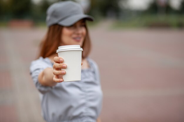 Tazza di carta bianca con caffè in mano della donna. tempo per bere un caffè in città. caffè da portar via. goditi il momento, prenditi una pausa. primo piano della tazza di carta usa e getta. bevanda calda deliziosa. spazio vuoto per testo, mockup