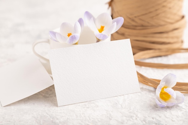 White paper invitation card mockup with purple crocus snowdrop
flowers on gray concrete background side view copy space