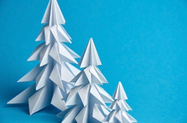 White paper origami christmas trees on blue