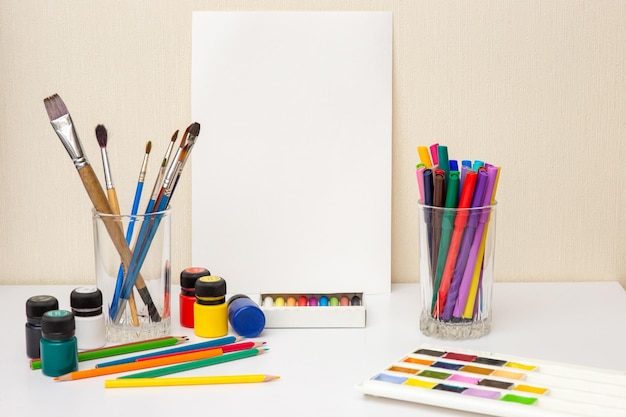 White paper paintbrushes and colorful drawing supplies on white table