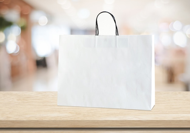 White paper shopping bag standing on wood table over blurred store with copy space