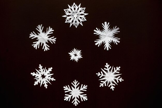 White paper snowflakes different shapes and sizes on brown cardboard background Top view