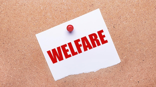 写真 welfare というテキストが記載されたホワイト ペーパーが、赤いボタンで木製の背景に取り付けられています。