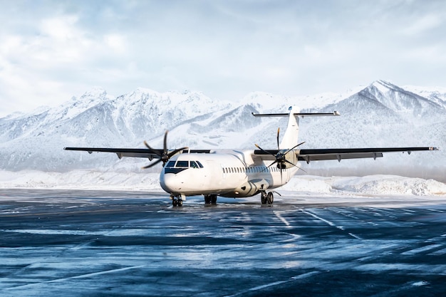 写真 高い景色の山を背景に冬の空港の停車場にある白い旅客ターボプロップ航空機