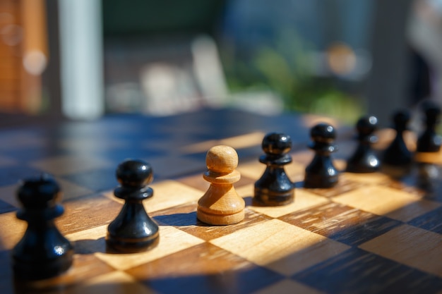 A white pawn between black chess pieces on an old chessboard. Leadership concept.