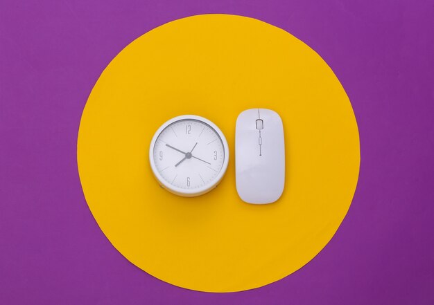 White pc mouse and clock on purple background with yellow circle. Conceptual studio shot. Minimalism. Top view