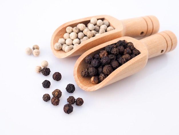 White pepper and black pepper in wooden spoon isolated on white surface.