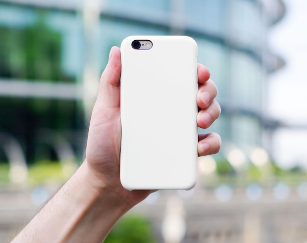 White phone case mock up on blurred city background in a man's hand