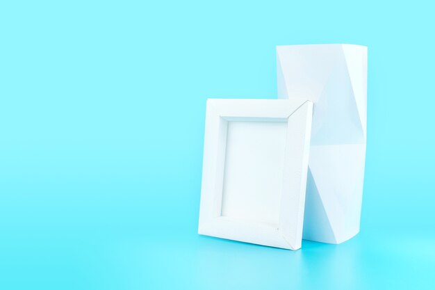 White photo frame(made from paper) and polygon vase on light blue background