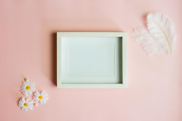 Photo white photo frame with feather and white flowers over the pink background