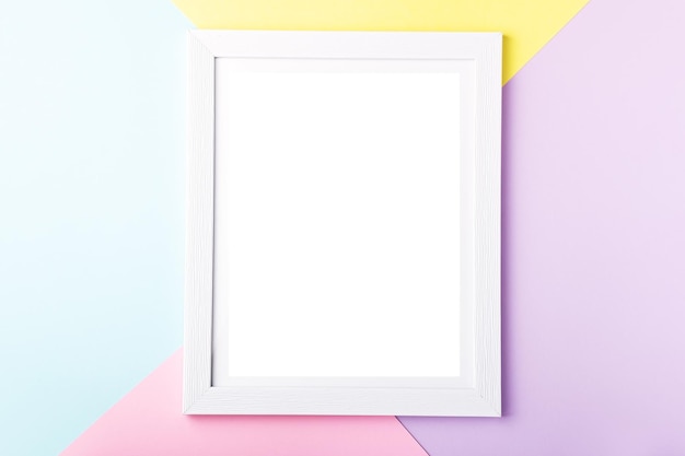 White picture frame on pastel pink yellow blue multicolor geometric background Mockup on colorful table top copy space top view