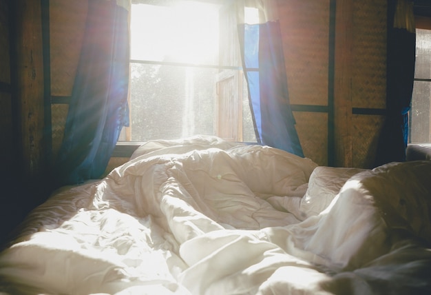 White pillows and bedding sheet in a clean hotel bedroom with morning view background