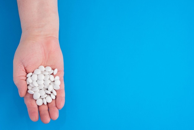 White pills are held in hand by an adult woman on a blue background