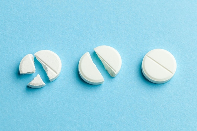 Белые таблетки на синем фоне Несколько таблеток разбиты пополам, уменьшая дозу лекарства