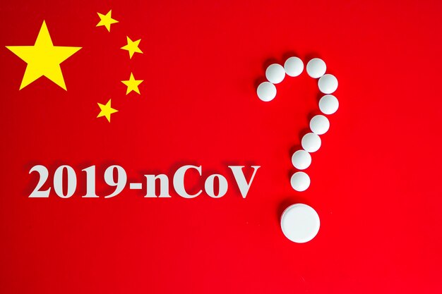 White pills in the form of a question mark on a red background with inscription 2019-nCoV and copy space for text. Red background of the Chinese flag. 2019 Novel Coronavirus 2019-nCoV concept.