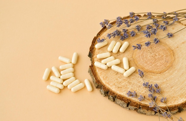 White pills lie on a wooden round podium next to lavender flowers a mockup of homeopathic products