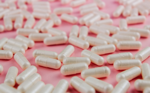 White pills on a pink wall. Scattered tablets.