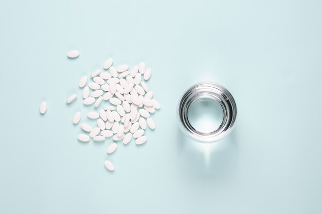 White pills with glass of clear water over blue table. Overhead shots