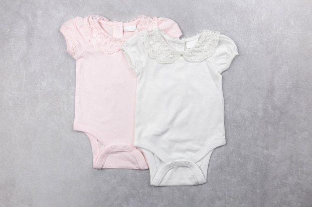 White and pink baby girl bodysuit mockup flat lay on the gray concrete surface