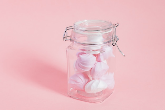 White and pink twisted meringues in a glass jar on pink background