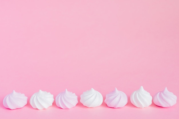 Photo white and pink twisted meringues in a row on pink background, greeting card, copy space