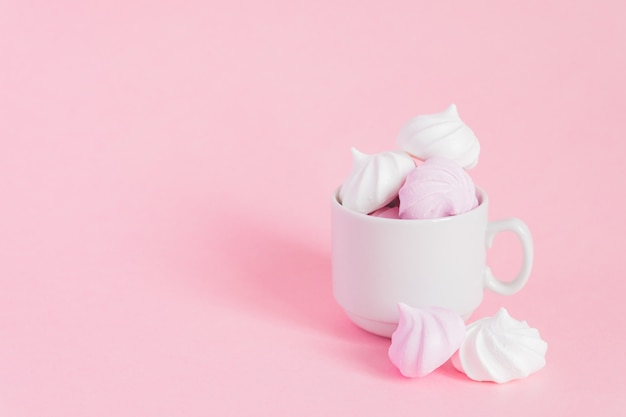 White and pink twisted meringues in a small porcelain coffee cup on pink backgroundwith copy space