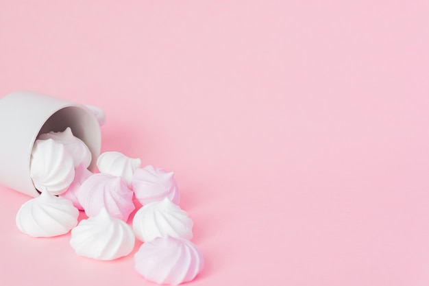 White and pink twisted meringues in a small porcelain coffee cup on pink