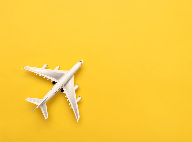 The white plane lies on a yellow background. Travel concept. Creative idea of flying on an airplane.