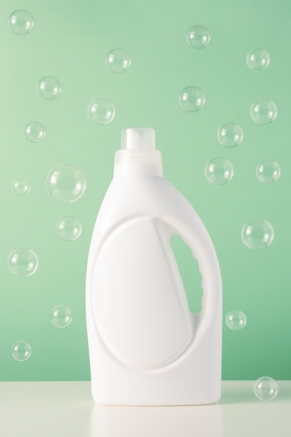 Photo white plastic bottle of liquid laundry detergent or bleach or fabric softener with flying bubbles. blank mockup packaging for cleaning agent on green background. laundry day