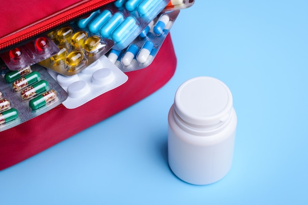 White plastic bottle near red bag with pills and capsules on a white 