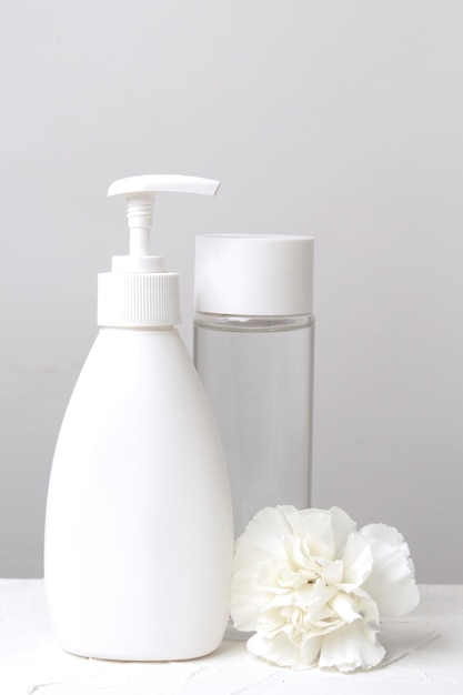 White plastic bottle with dispenser closeup with white flower on a white background