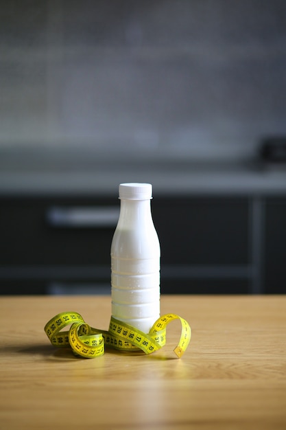 White plastic bottle with a measuring tape on a wooden table with blurred kitchen background