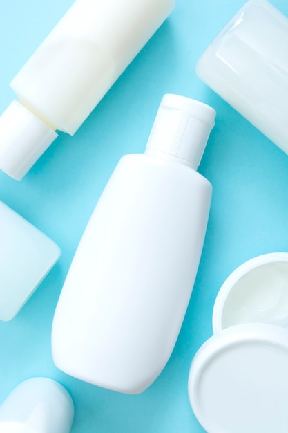 White plastic cosmetic bottles on blue background, skin and body care, top view flatlay, vertical image