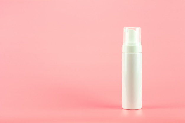 White plastic cosmetic lotion bottle on pink background.