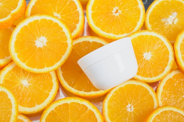 White plastic cream jar over sliced oranges backgronund, top view