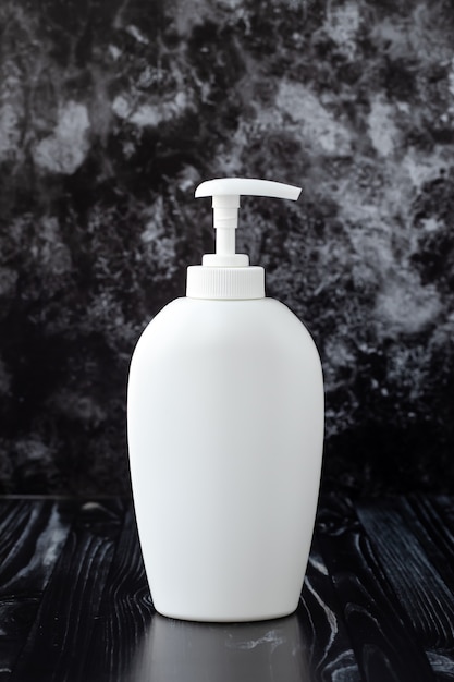 White plastic dispenser bottle with liquid soap on black marble wall. Hygiene concept.