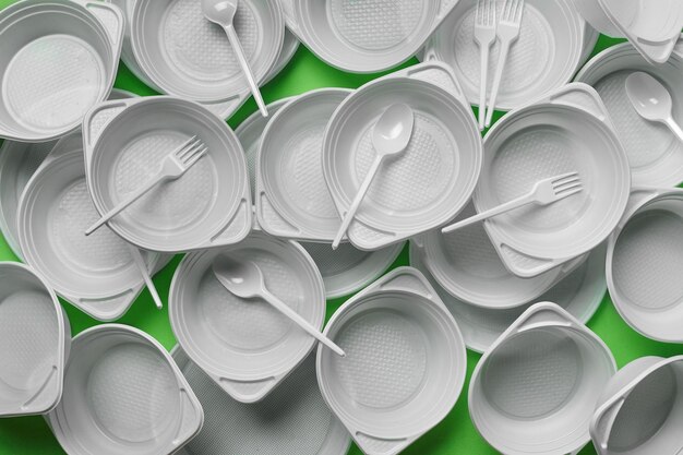 White plastic disposable tableware on green background with copy space The concept of picnic utensil Top view Selective focus Closeup