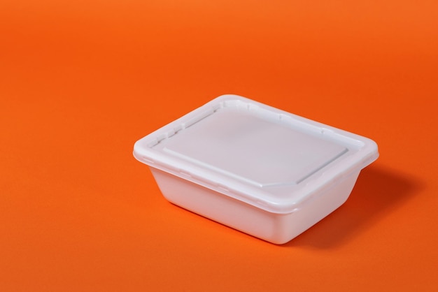 White plastic fast food box on orange background - side view, isolate