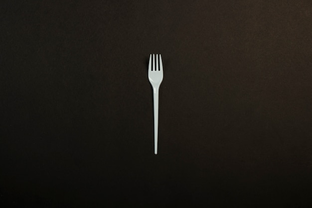 White plastic fork on a black background. Concept plastic, harmful, environmental pollution, stop plastic. Flat lay, top view.