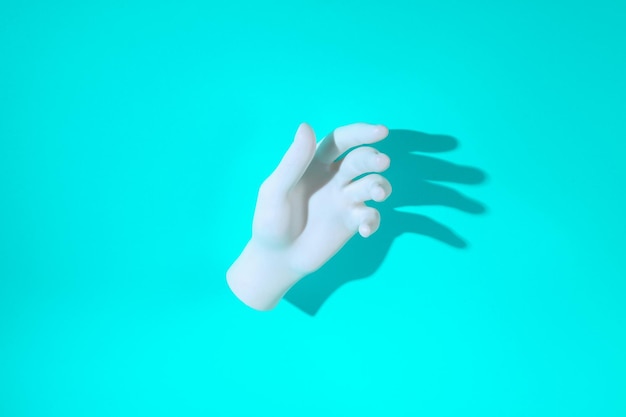 Photo white plastic hand on a turquoise background with a long shadow minimal layout