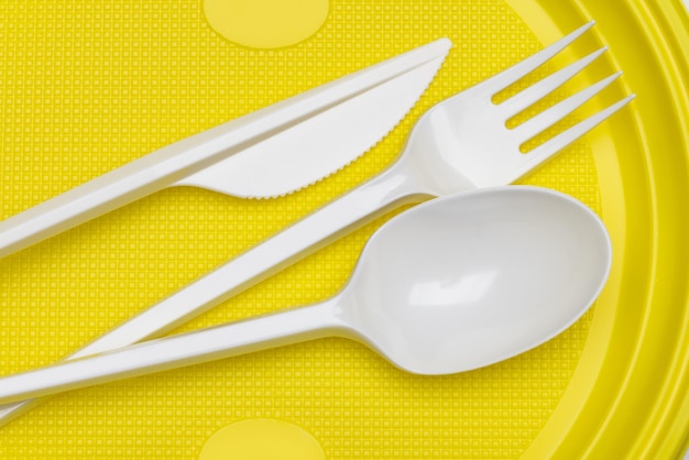 Photo white plastic knife, fork and spoon on a yellow background.