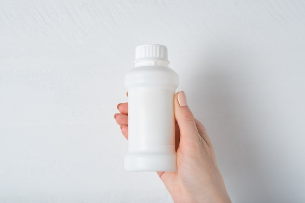 White plastic medicine bottle in a female hand. White background