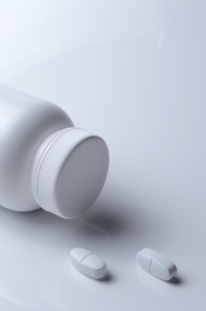 White plastic medicine jar and two white pills light background