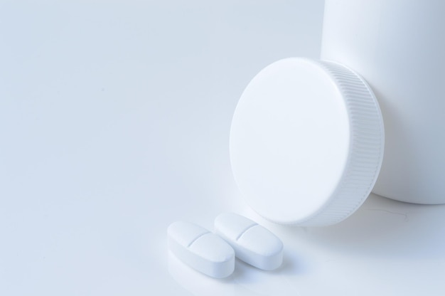 White plastic medicine jar and two white pills light background