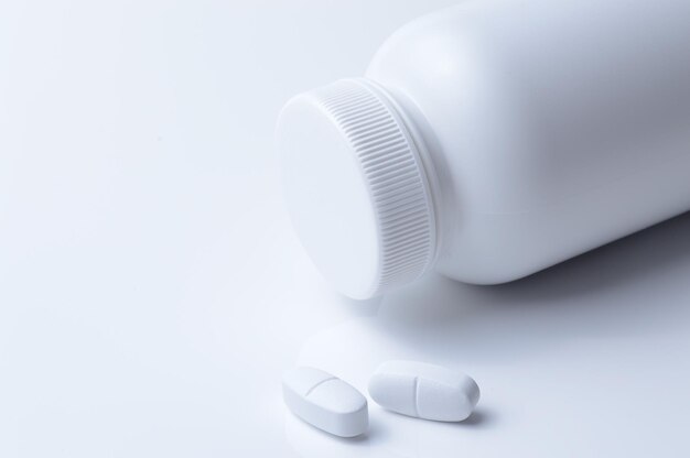 White plastic medicine jar and two white pills light background